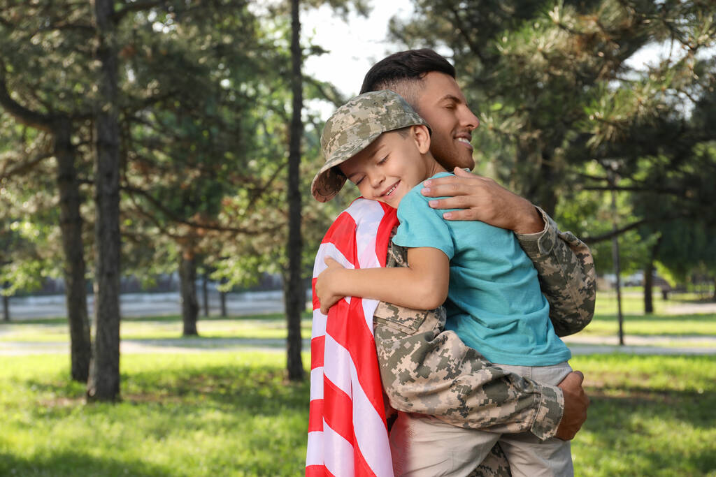 Soldaat met vlag van USA en zijn zoontje knuffelend buiten - Foto, afbeelding