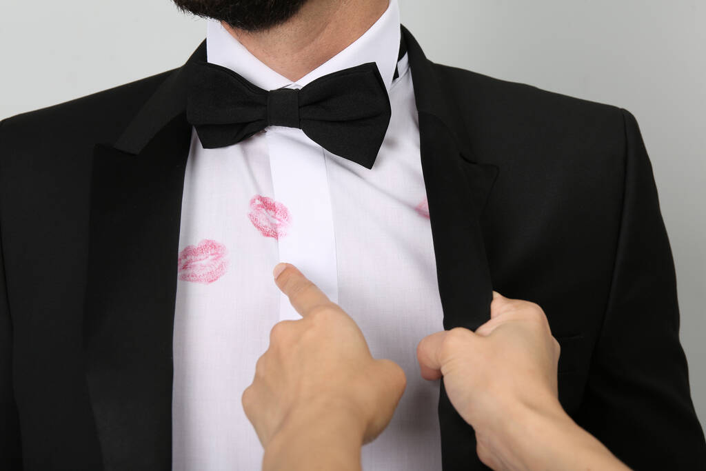 Mujer señalando marcas de beso de lápiz labial en la camisa de su marido sobre fondo blanco, primer plano - Foto, Imagen