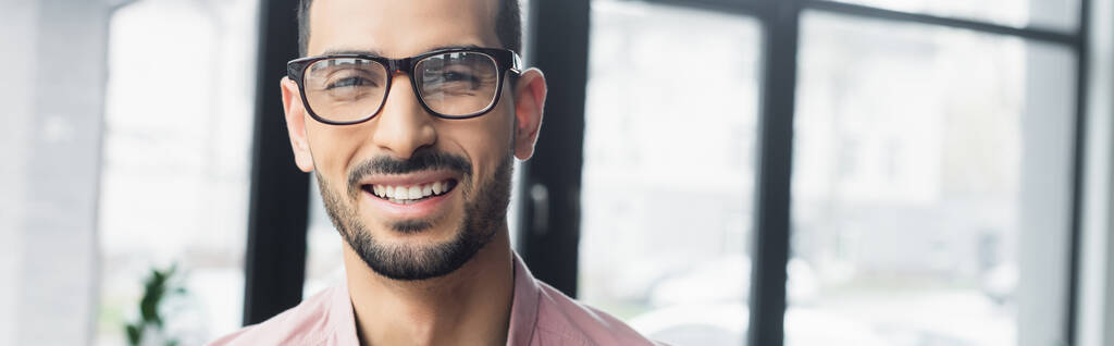 Vrolijke moslim zakenman in bril kijkend naar camera op kantoor, spandoek  - Foto, afbeelding