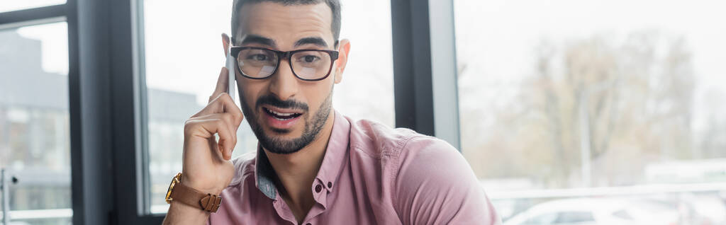 Mladý arabský podnikatel v brýlích mluví na mobilním telefonu v kanceláři, banner  - Fotografie, Obrázek