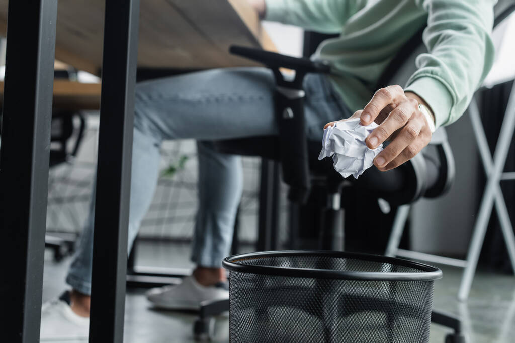 Gekropte weergave van wazige zakenman die verkreukeld papier in de buurt van prullenbak in kantoor houdt  - Foto, afbeelding