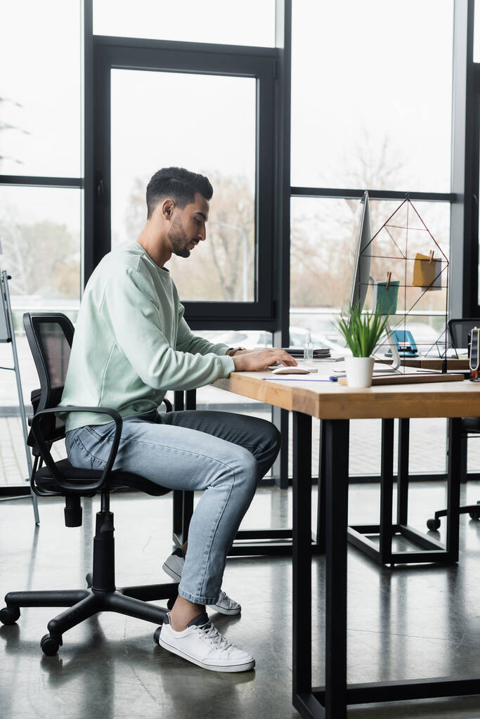 Вид сбоку на арабского бизнесмена в повседневной одежде с помощью компьютера во время работы в офисе  - Фото, изображение