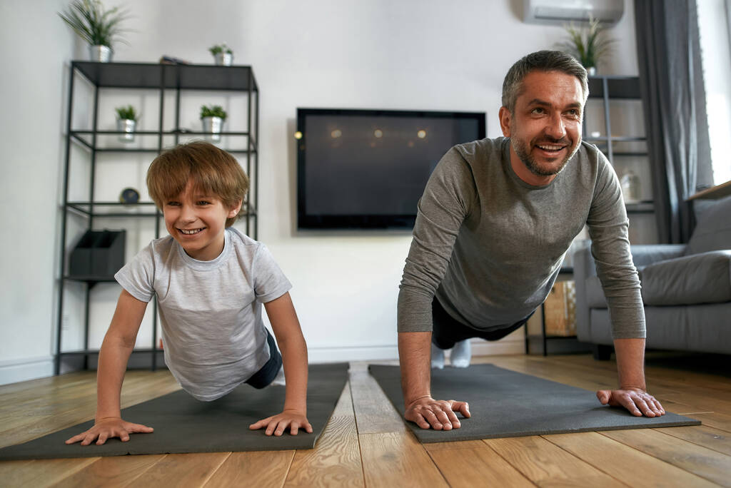 Smiling active dad and son exercise train together at home - Photo, Image