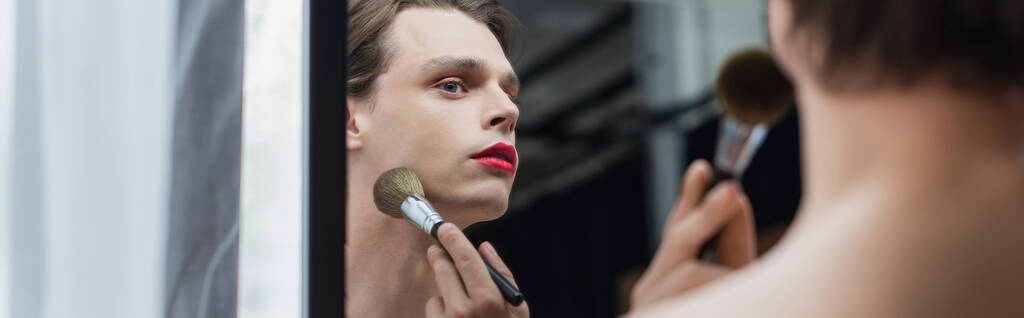 νεαρός τρανσέξουαλ άνθρωπος εφαρμογή σκόνη προσώπου στο λαιμό κοντά στον καθρέφτη, πανό - Φωτογραφία, εικόνα