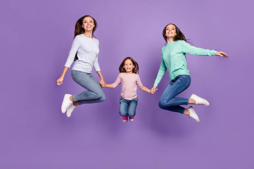 Повний розмір тіла трьох досить модних веселих дівчат, які стрибають, тримаючи руки ізольовані на яскраво-фіолетовому фіолетовому кольоровому фоні
 - Фото, зображення