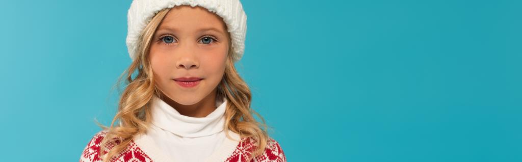 girl in knitted hat looking at camera isolated on blue, banner - Photo, Image