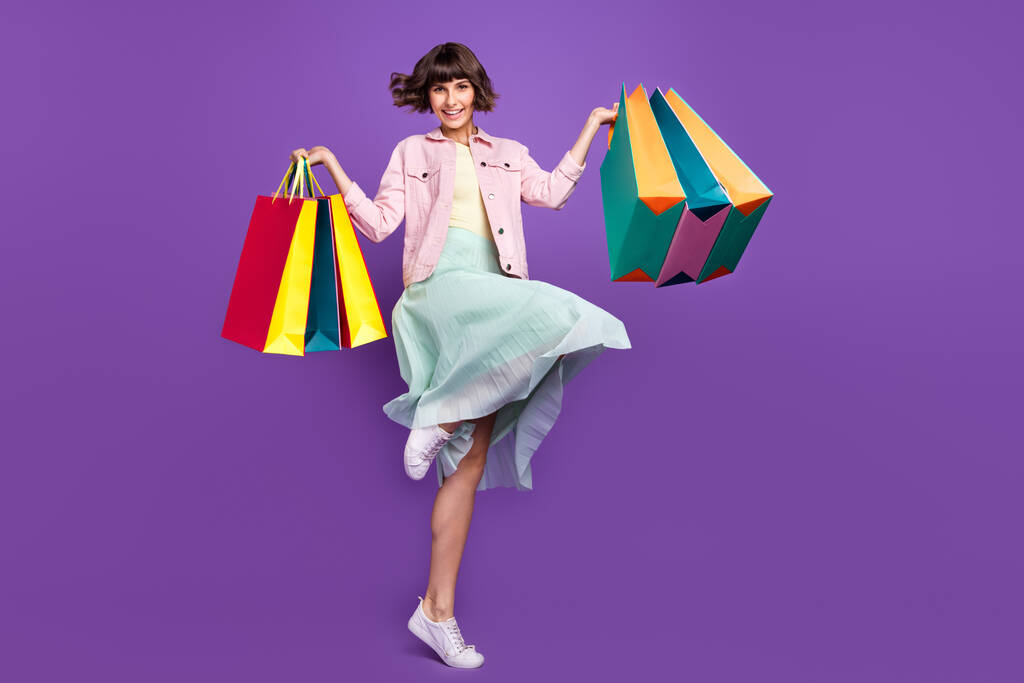Фотография в полный рост жизнерадостной молодой женщины, держащей за руки сумки покупателя, с улыбкой на фоне фиолетового цвета - Фото, изображение