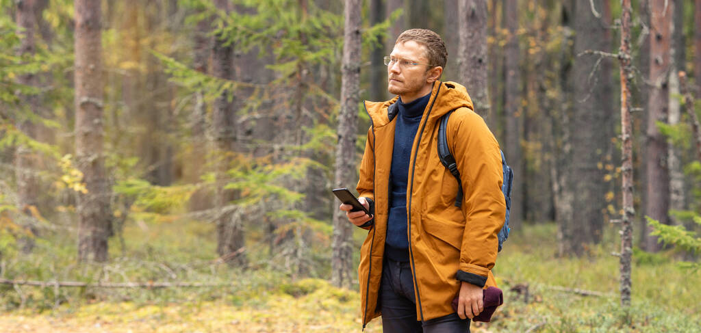 Мужчина средних лет со смартфоном в хвойном осеннем лесу. Турист - человек походы в лес - Фото, изображение