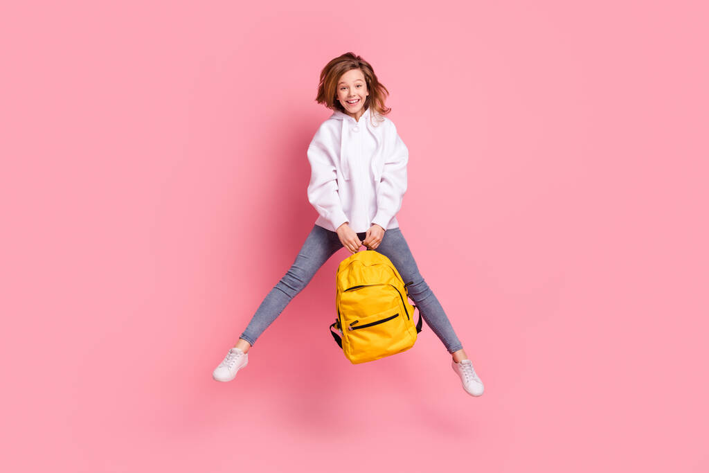 Volledige lengte lichaam grootte meisje springen omhoog houden schooltas blij vrolijk geïsoleerd pastel roze kleur achtergrond - Foto, afbeelding