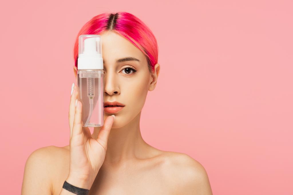 татуйована молода жінка з барвистим волоссям, що тримає пляшку з очищувальним продуктом, прикриваючи очі ізольовано на рожевому
  - Фото, зображення