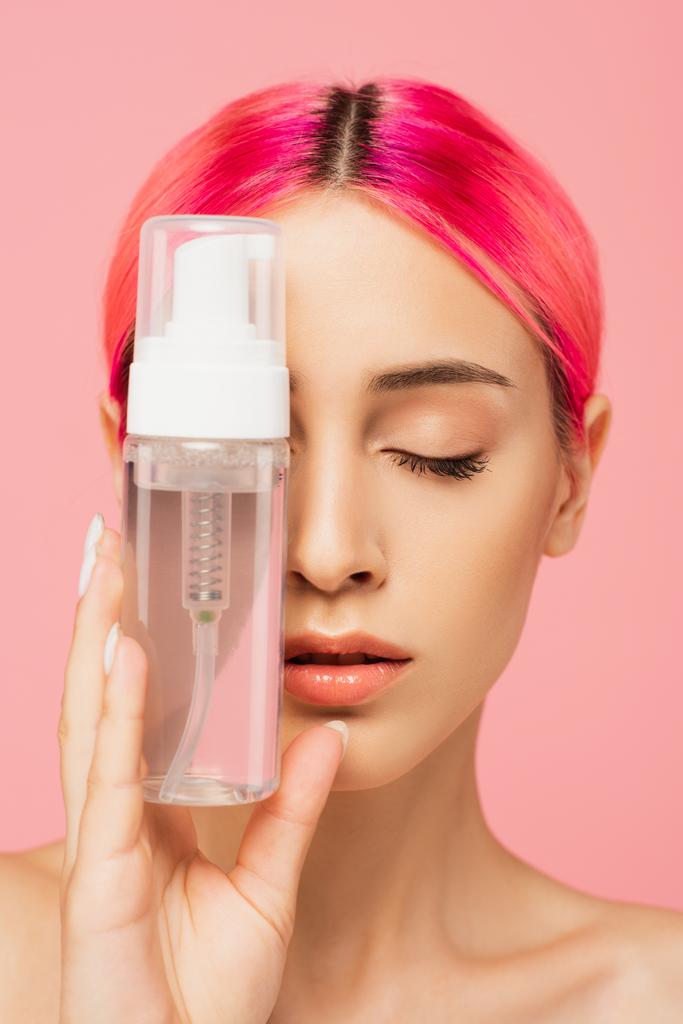 jeune femme aux cheveux colorés et les yeux fermés tenant bouteille avec produit nettoyant isolé sur rose  - Photo, image