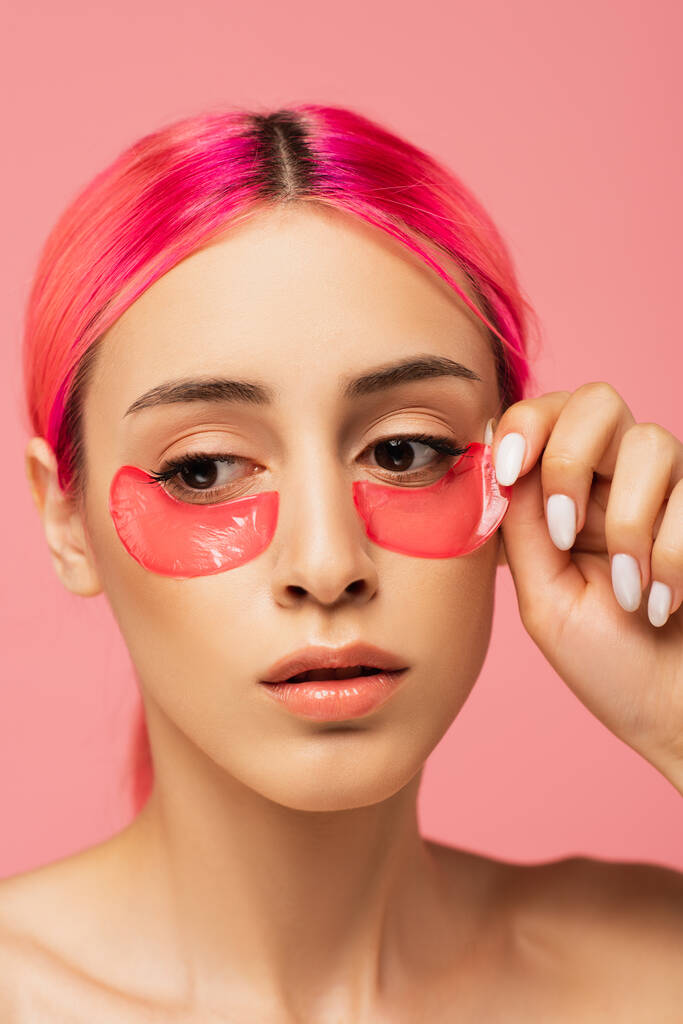 jeune femme aux cheveux colorés appliquant des patchs collagène pour les yeux isolés sur rose  - Photo, image