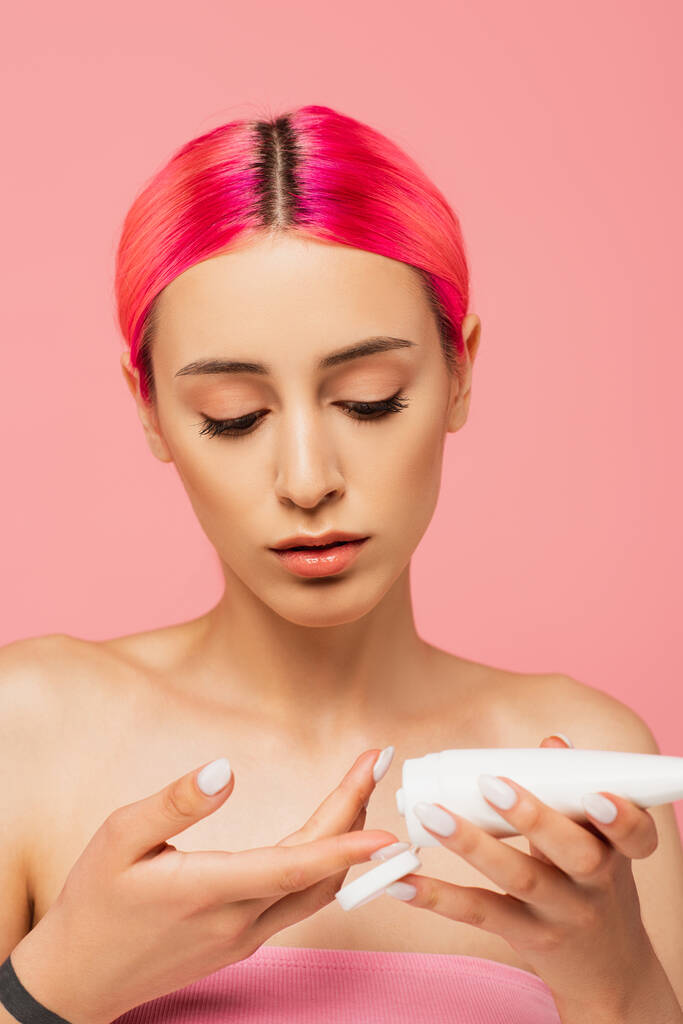 mujer joven con tubo de retención de pelo colorido mientras se aplica el producto cosmético aislado en rosa  - Foto, imagen