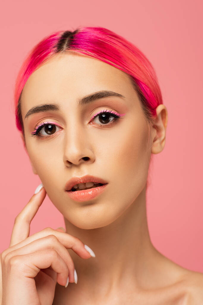 hübsche junge Frau mit bunten Haaren blickt vereinzelt in die Kamera auf rosa  - Foto, Bild