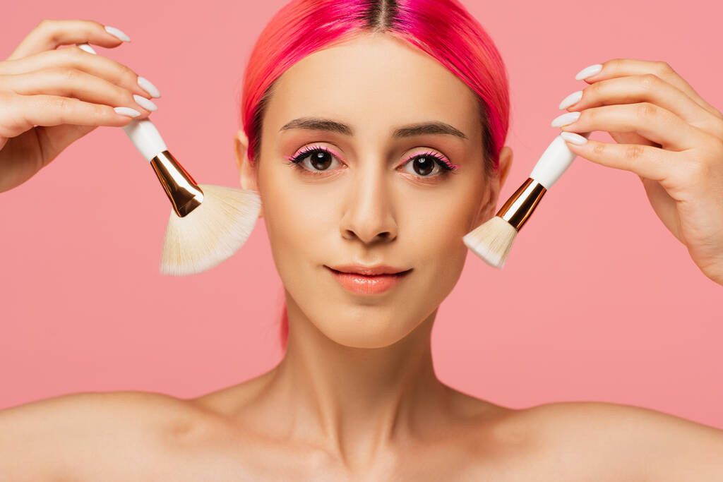 junge Frau mit gefärbten Haaren hält Kosmetikpinsel isoliert auf rosa  - Foto, Bild