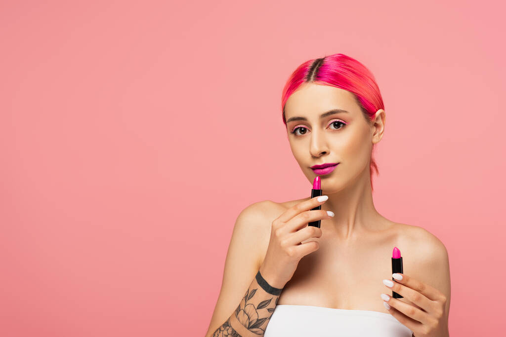 jonge vrouw met kleurrijke haar houden lipsticks geïsoleerd op roze  - Foto, afbeelding
