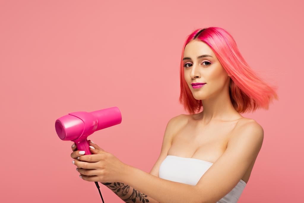 bonita mujer joven con pelo colorido sosteniendo secador de pelo aislado en rosa  - Foto, Imagen