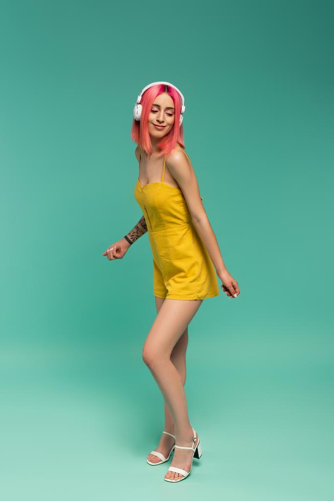 full length of happy νεαρή γυναίκα με ροζ βαμμένα μαλλιά ακούγοντας μουσική στα ακουστικά, ενώ χορεύουν σε μπλε - Φωτογραφία, εικόνα