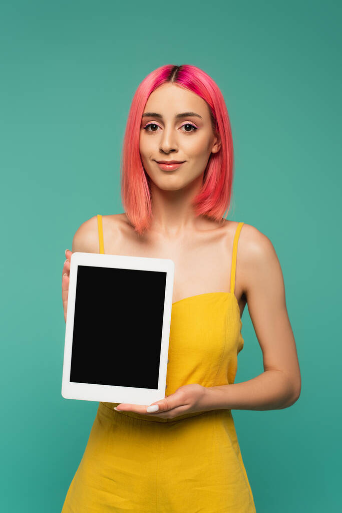 joven sonriente con cabello teñido de rosa sosteniendo tableta digital con pantalla en blanco aislada en azul  - Foto, imagen