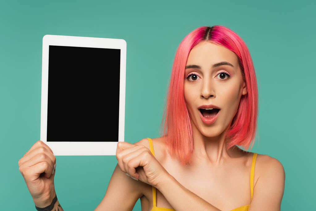 ピンク色の髪をした若い女性が青い画面で孤立したデジタルタブレットを持っています  - 写真・画像
