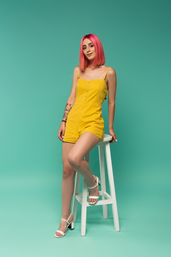full length of happy young woman with pink dyed hair sitting on stool on blue  - Photo, Image