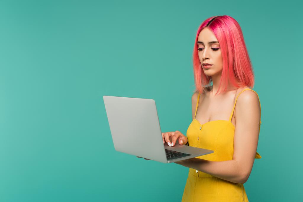 jeune femme avec des cheveux teints en rose à l'aide d'un ordinateur portable isolé sur bleu  - Photo, image