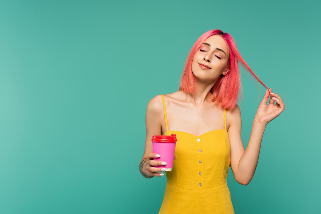 pleased young woman holding paper cup and adjusting pink dyed hair isolated on blue  - Photo, Image