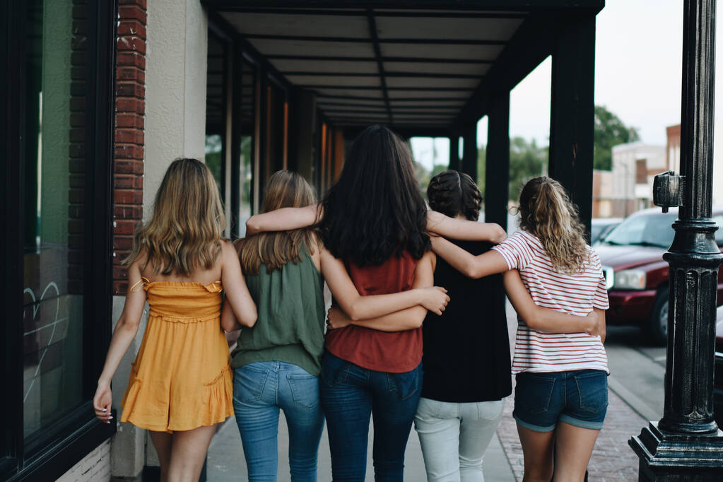 Una vista trasera de un grupo de amigas abrazándose y caminando al aire libre - Foto, imagen