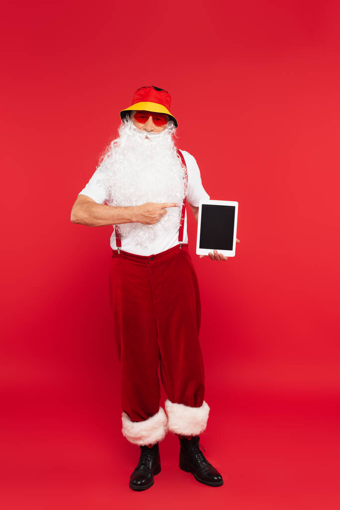 Joulupukki Panamassa ja aurinkolasit osoittavat digitaaliseen tablettiin punaisella taustalla - Valokuva, kuva
