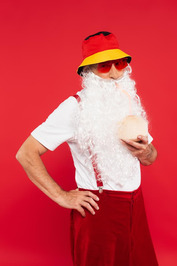 Güneş gözlüklü ve panamalı Noel Baba hindistan cevizli kokteyl tutuyor. Kırmızı renkte.  - Fotoğraf, Görsel