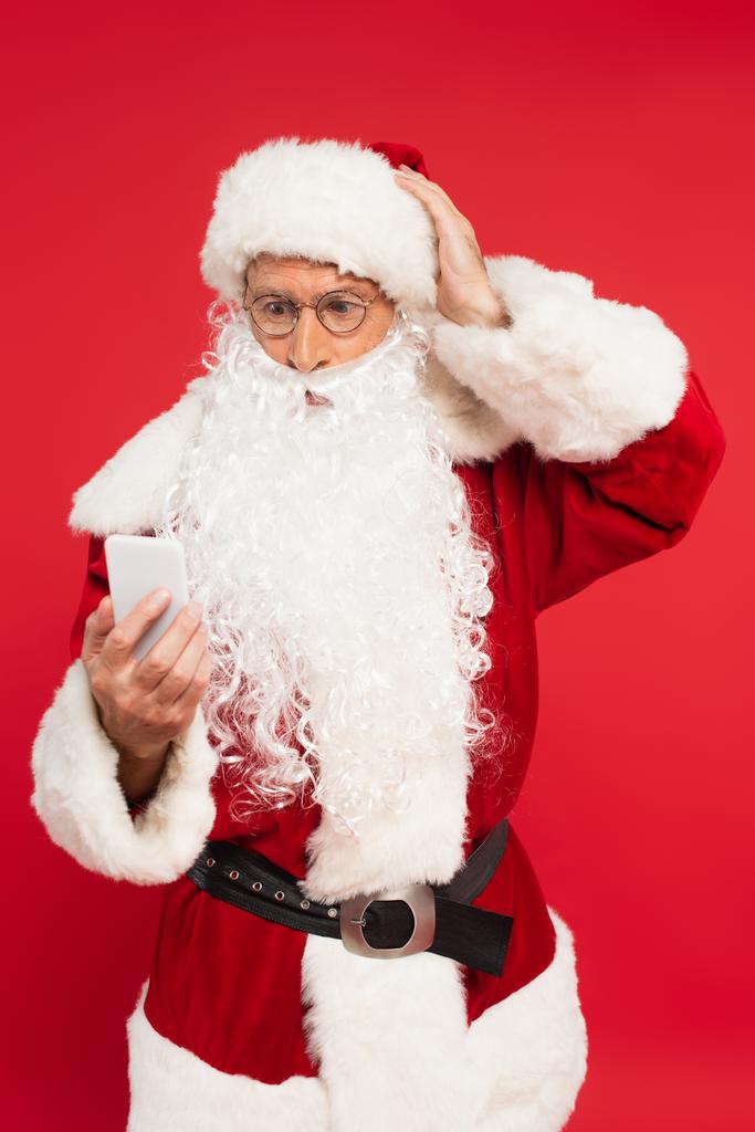 Kırmızı ışıkta izole edilmiş akıllı telefon kullanan endişeli Noel Baba.  - Fotoğraf, Görsel