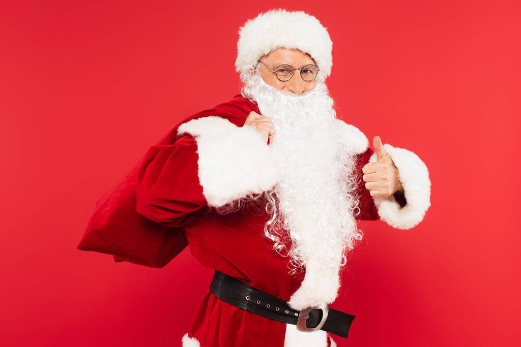 Kerstman in kostuum houden zak en tonen als geïsoleerd op rood  - Foto, afbeelding