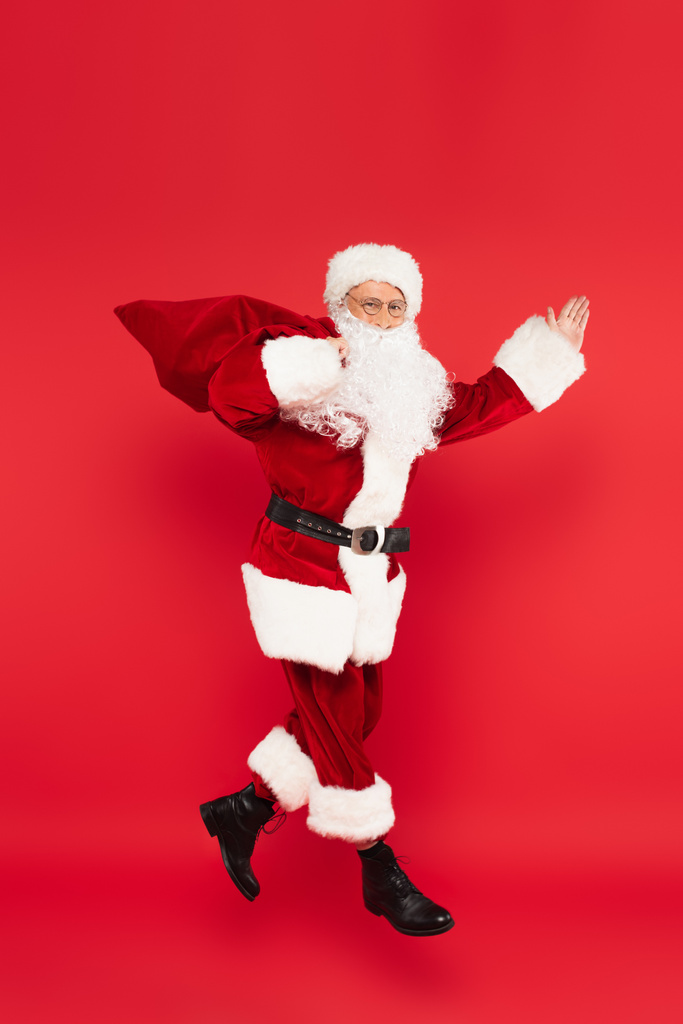 Санта-Клаус с мешком указывая рукой и левитации изолированы на красный  - Фото, изображение