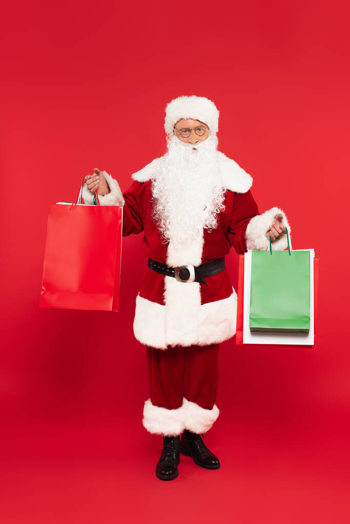 サンタクラウスで衣装や眼鏡を保持ショッピングバッグ上の赤の背景 - 写真・画像