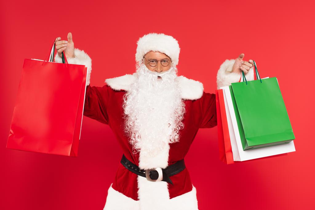 Father christmas holding shopping bags isolated on red  - Photo, Image