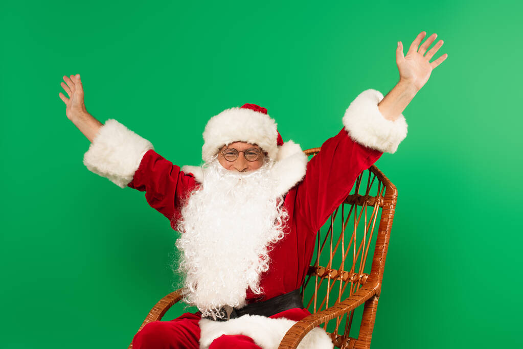 Opgewonden kerstman zit op schommelstoel geïsoleerd op groen - Foto, afbeelding