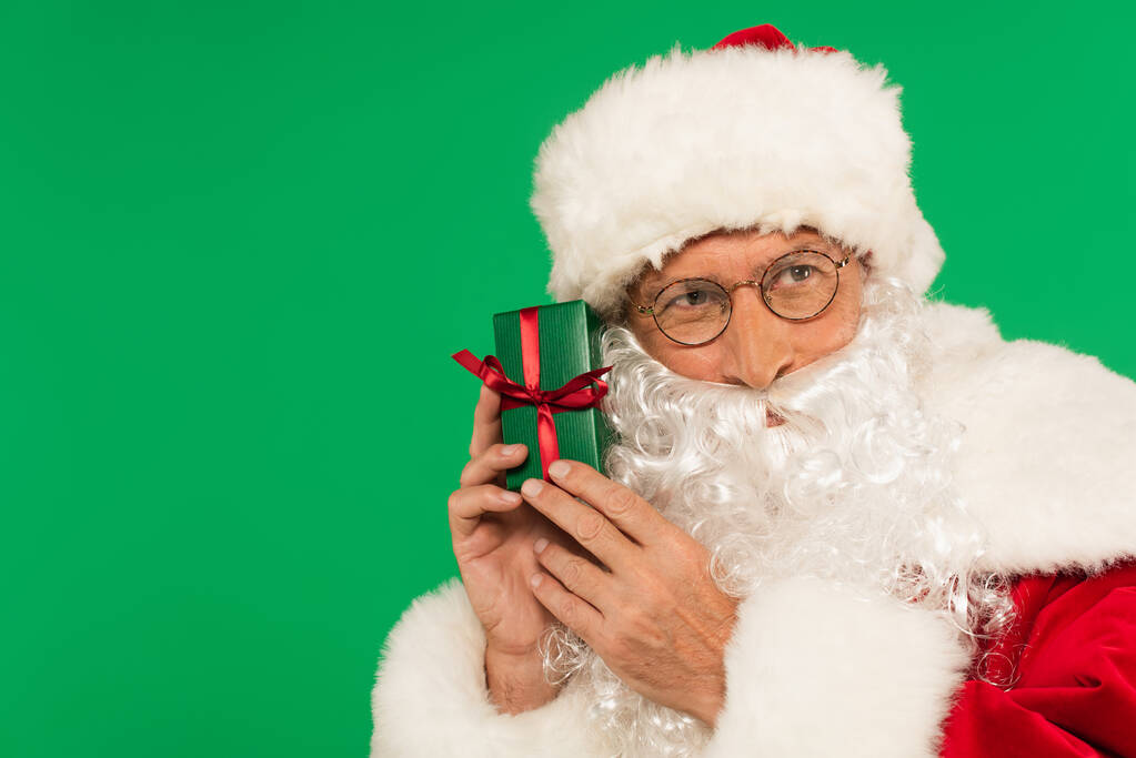 Święty Mikołaj w okularach trzymając pudełko z wstążką izolowane na zielono - Zdjęcie, obraz