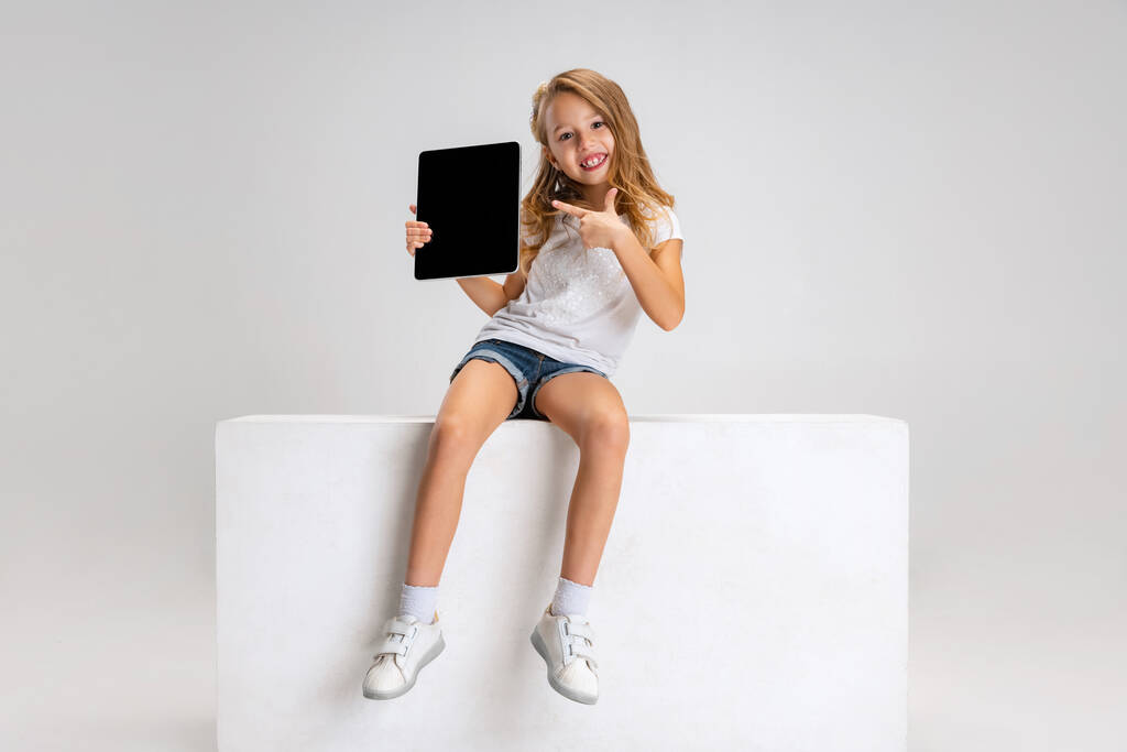 Retrato de una niña linda con ropa casual sentada en una caja grande aislada en un fondo de estudio blanco. Concepto de infancia feliz. - Foto, Imagen