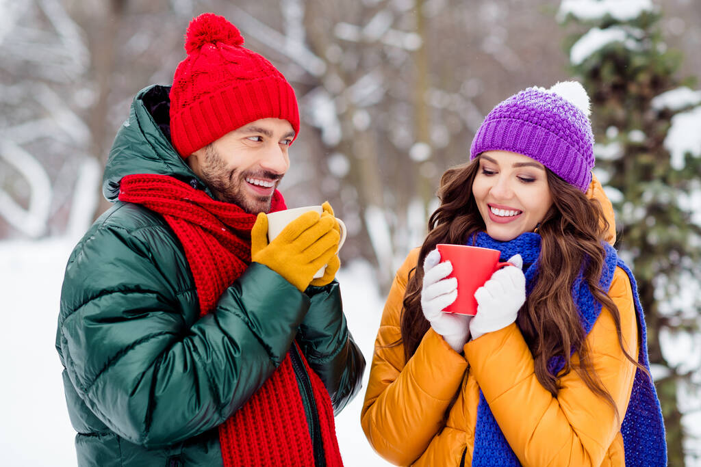 Foto van charmant mooi huwelijk koppel dragen windbreakers glimlachend drinken koffie wandelen besneeuwd weer buiten park - Foto, afbeelding