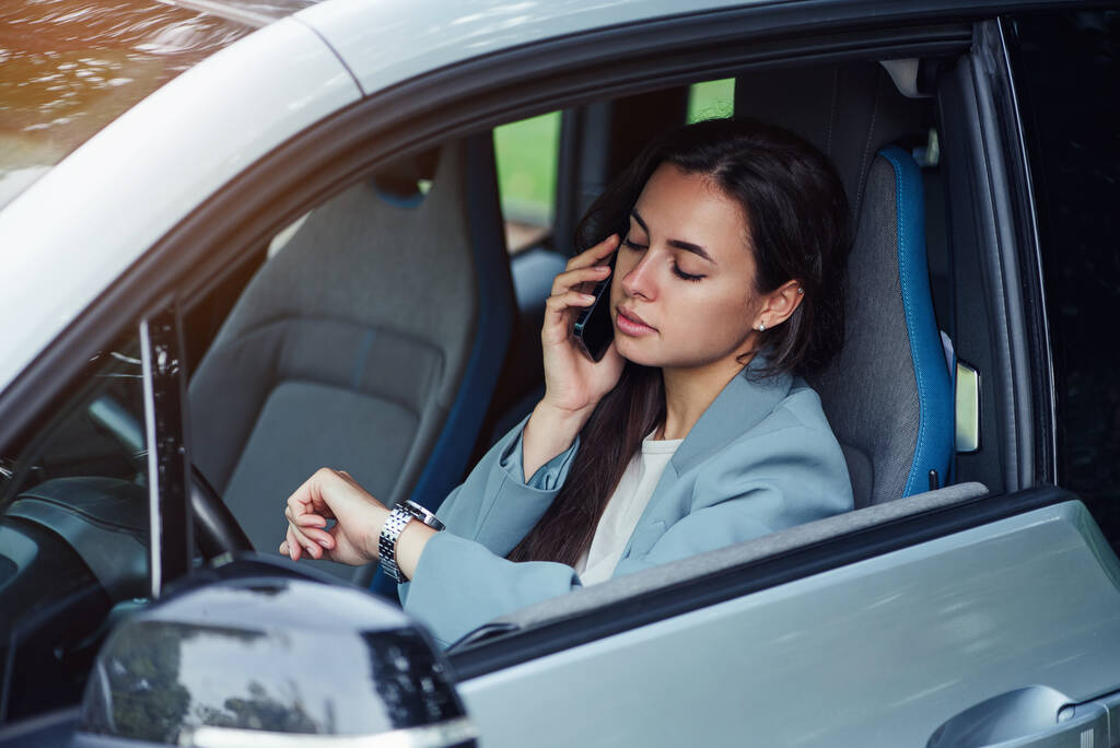 Attractive young woman speaks on mobile phone while sitting in the car. Portrait of a young business woman. - Photo, Image
