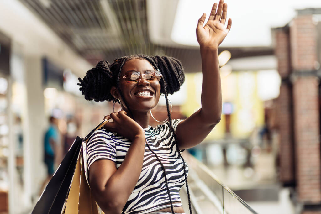 Porträt einer lächelnden jungen schwarzen Frau, die eine Brille trägt, Einkaufstüten in der Hand hält, Einkaufszentrum, Einkaufskonzept, Konsum - Foto, Bild
