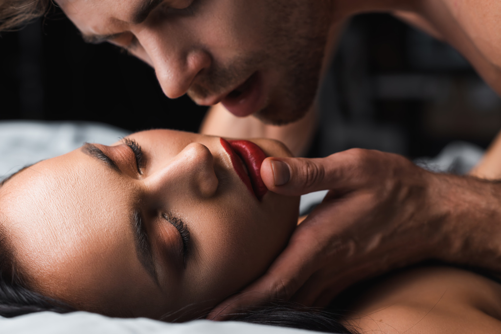 Homme touchant femme sexy avec les yeux fermés sur le lit sur fond noir  - Photo, image