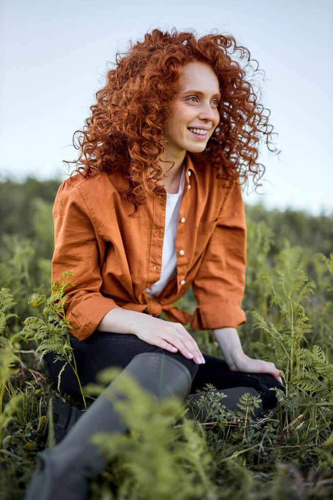Sonriendo inspirada calma dama sentada en verde hierba en campo en contemplación - Foto, Imagen