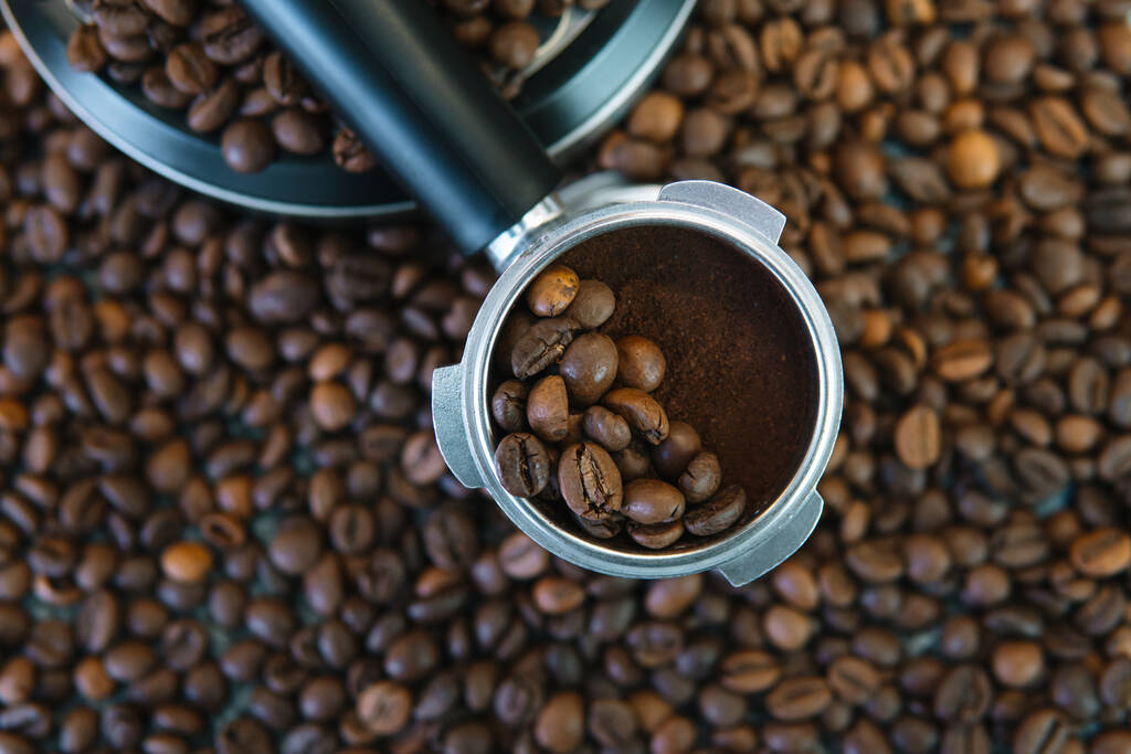 Porte-filtre machine à café expresso avec grains de café. Dans une moitié il y a des grains entiers, et dans l'autre moitié du café moulu - Photo, image