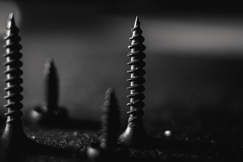 Een grijs shot van een stapel bouten en moeren op een donkere wazige achtergrond - Foto, afbeelding