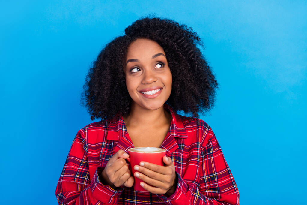 Fotografie relax mladá dáma pít kávu vypadat prázdný prostor nosit červené kostkované pyžama izolované na modrém pozadí - Fotografie, Obrázek