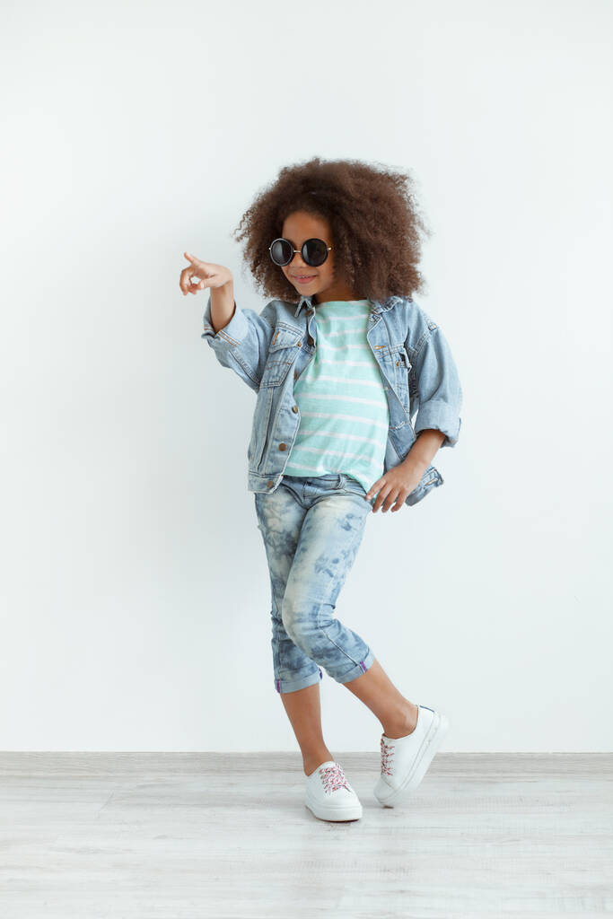 Забавная стильная девушка с красивыми вьющимися волосами в джинсовой одежде и солнечных очках - Фото, изображение