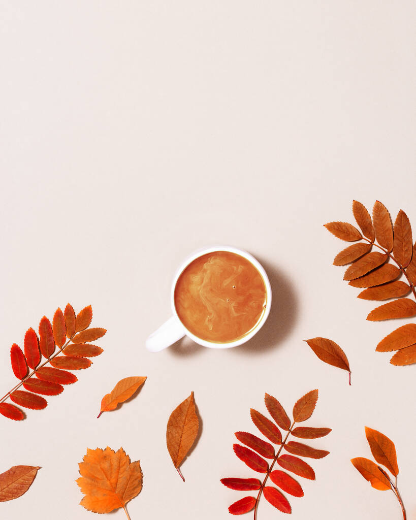 Filiżanka kawy z mlekiem i czerwonymi jesiennymi liśćmi na pastelowym różowym tle papieru. Jesień, kompozycja jesienna, monobloki płaskie, widok z góry, przestrzeń do kopiowania. - Zdjęcie, obraz