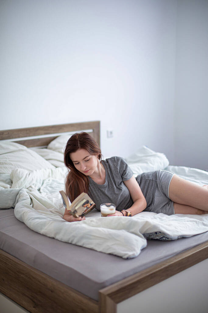Διαβάζοντας ένα βιβλίο λευκό κορίτσι με σκούρα μαλλιά στο κρεβάτι - Φωτογραφία, εικόνα