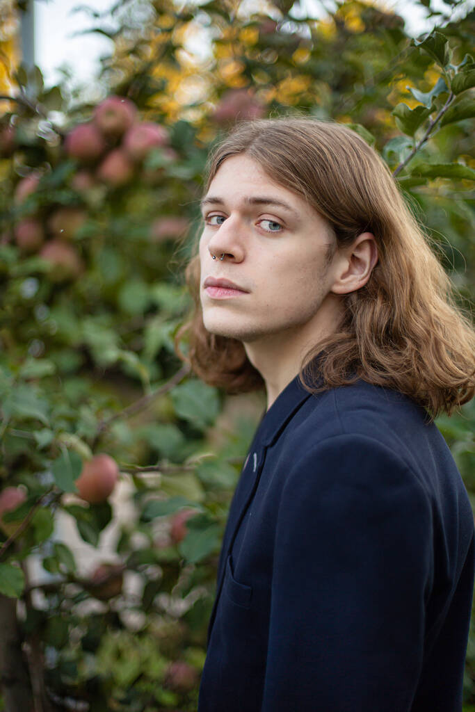 Білий молодий європеєць з довгим волоссям біля дерева з яблуками. - Фото, зображення